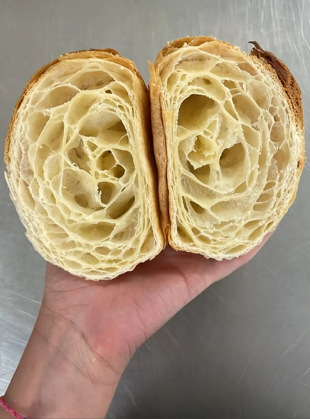 A croissant cut open in a hand, showing its laminated layers
