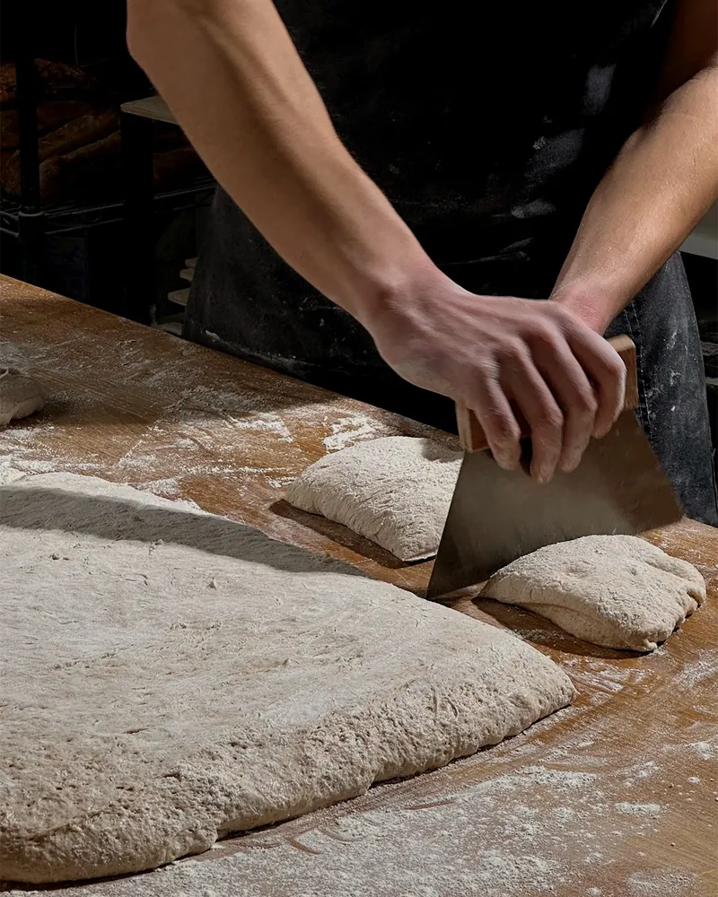 A baker cutting ciabatta dough on the table
